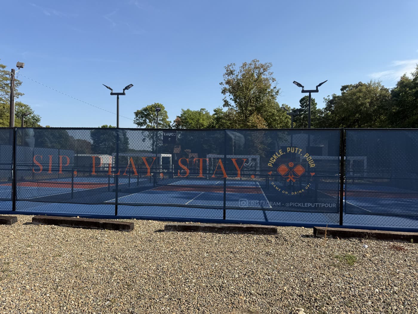 Pickle Putt Pour's pickleball court fence with a windscreen reading Sip Play Stay